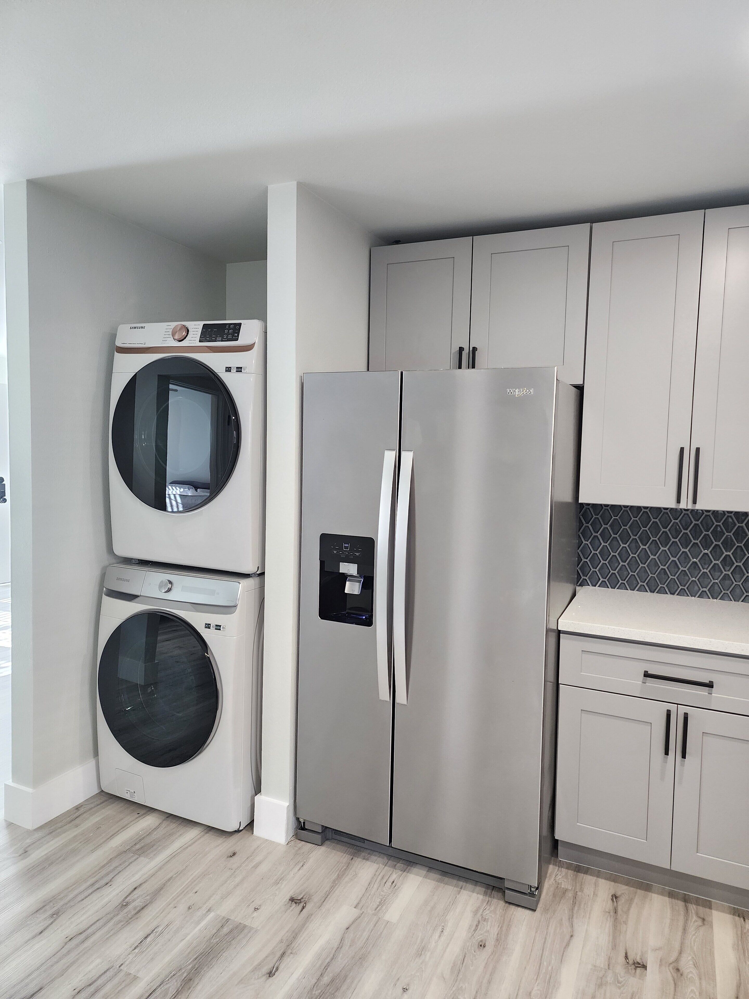 A compact kitchen with a stainless steel refrigerator, a built-in washer and dryer, and light grey cabinetry.