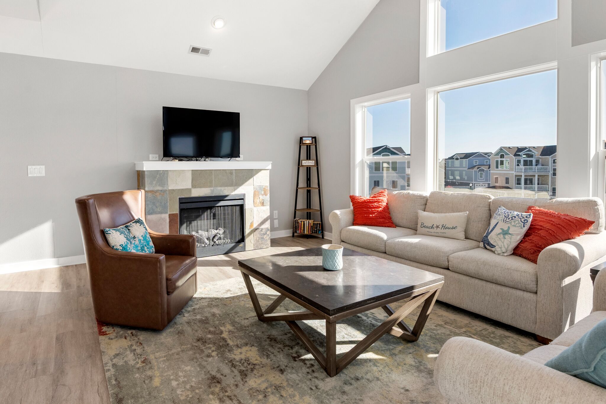 A living room with a fireplace, a television, and a large window with a view of houses.