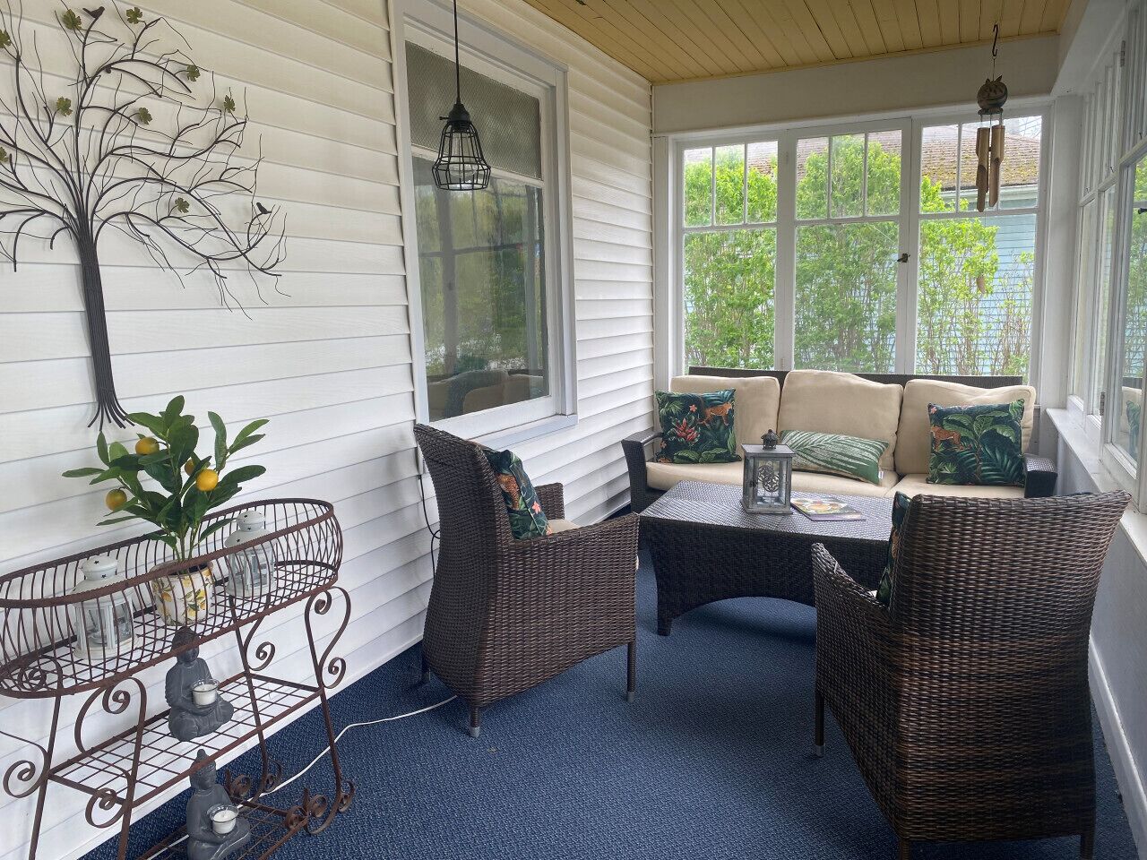 A sunroom with wicker furniture, a metal plant stand, and a view of greenery outside.