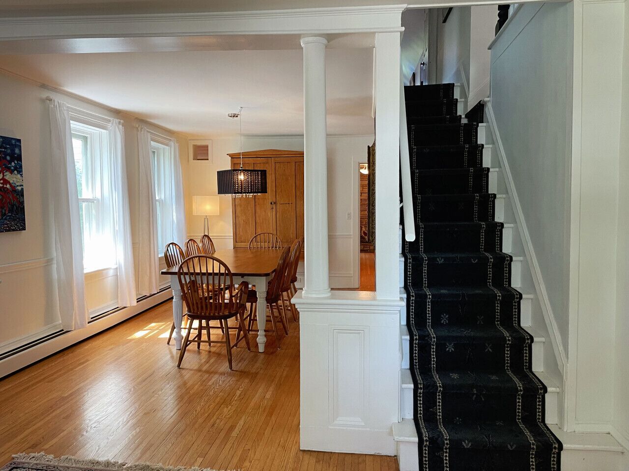 A spacious living area with a dining table and chairs, a staircase, and a kitchen in the background.
