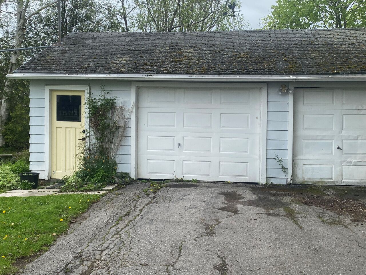 Un bâtiment d’un seul étage, doté d’une porte de garage, d’une petite porte d’entrée et d’une allée en béton.