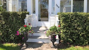 A house with a white exterior, a number '348' on the door, and a front porch with potted plants. - Spacious & Charming Century Home - Wellington (Prince Edward)