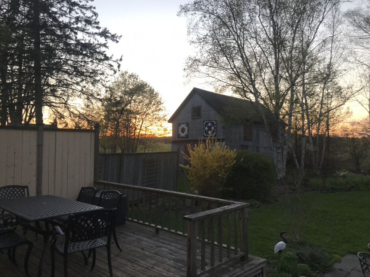 A wooden deck with a table and chairs, a small shed, and a grassy yard with trees.