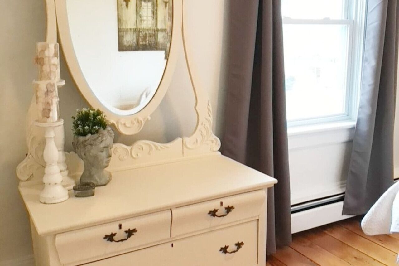 A white dresser with a mirror, two drawers, and a small plant.