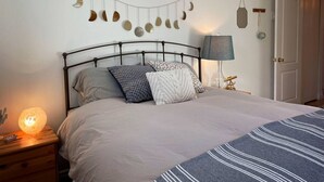 A neatly made bed with a patterned bedspread, a string of moon-shaped decorations on the wall, and a bedside lamp. - Relax in Style & Comfort in South Bay, PEC (Prince Edward)