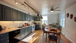 A modern kitchen with grey cabinets, a wooden dining table, and a ceiling fan. - Relax in Style & Comfort in South Bay, PEC (Prince Edward)