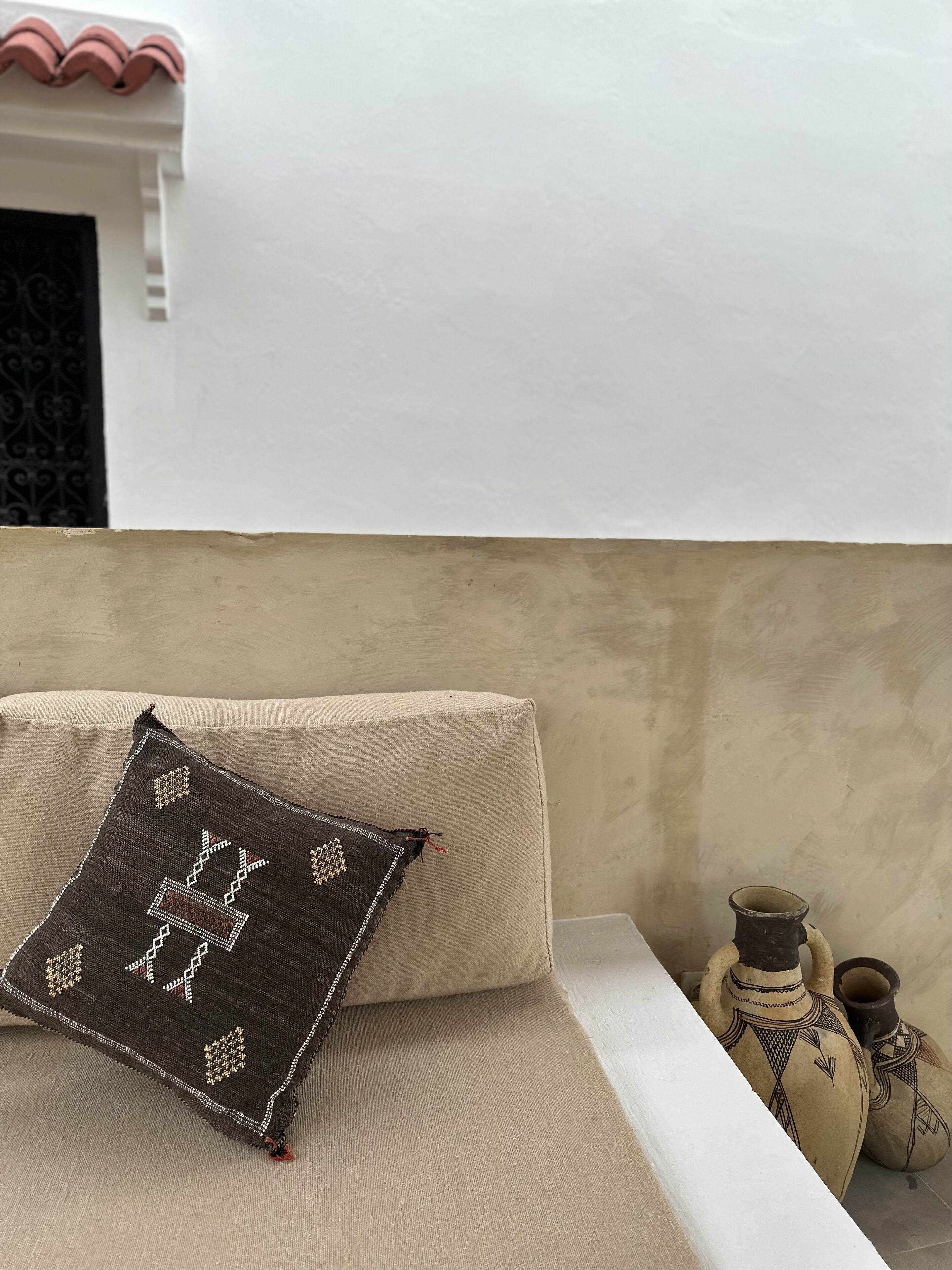 Un canapé beige agrémenté d’un coussin décoratif et de deux objets en céramique, le tout placé devant un mur uni.