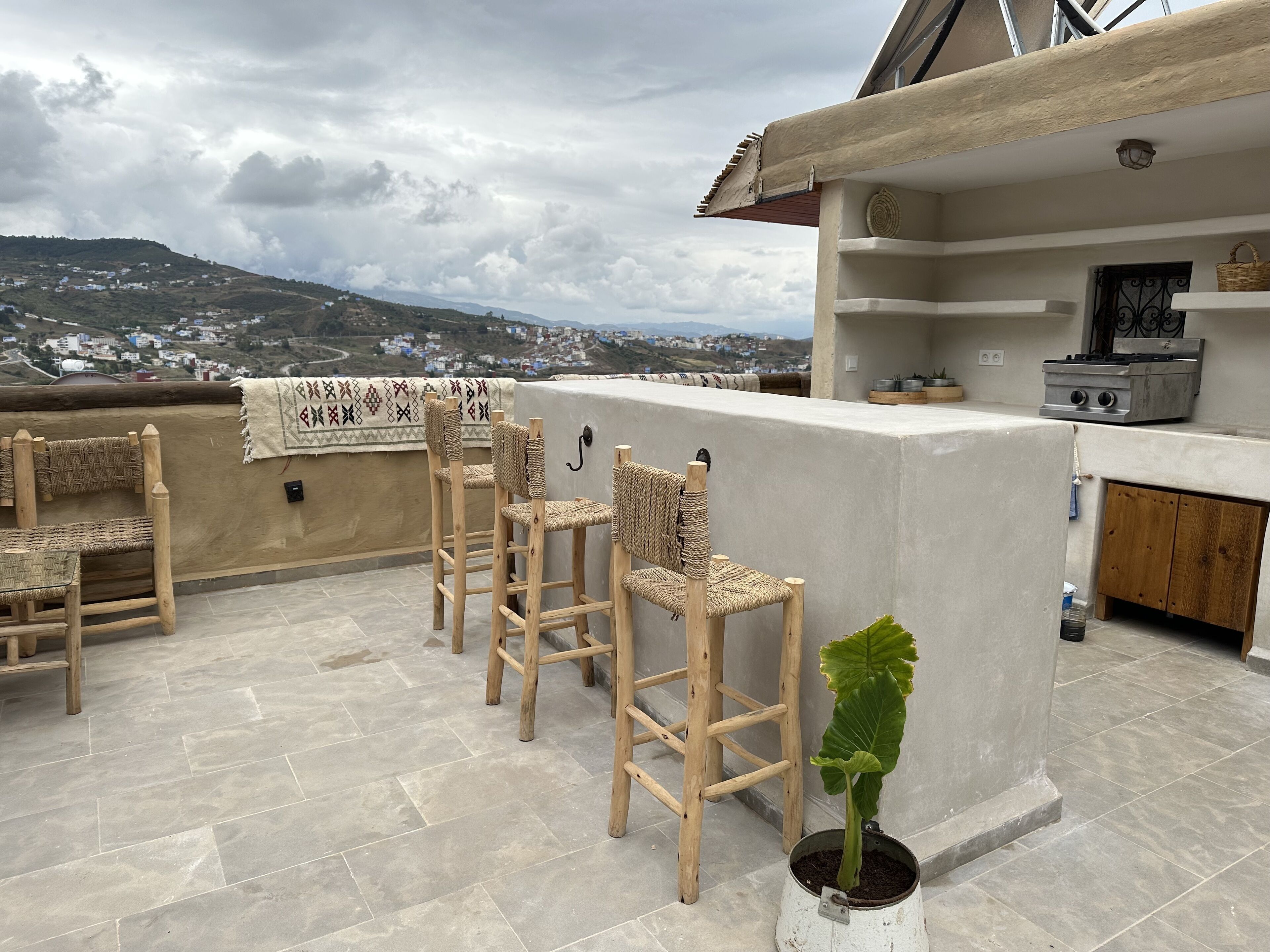 A rooftop terrace with a seating area, a potted plant, and a kitchen area with a stove.