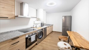A compact kitchen with a built-in oven, washing machine, and a stainless steel refrigerator.