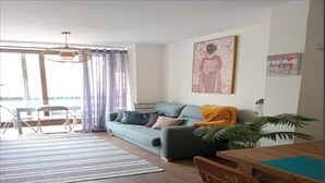 A modern living room with a sofa, a dining table, and a large window with curtains.