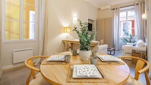 A dining area with a round wooden table set for four, surrounded by wooden chairs. A potted plant is in the center, and there are two wall-mounted lamps. - Elegant flat with AC, heart of Nice (Nice)