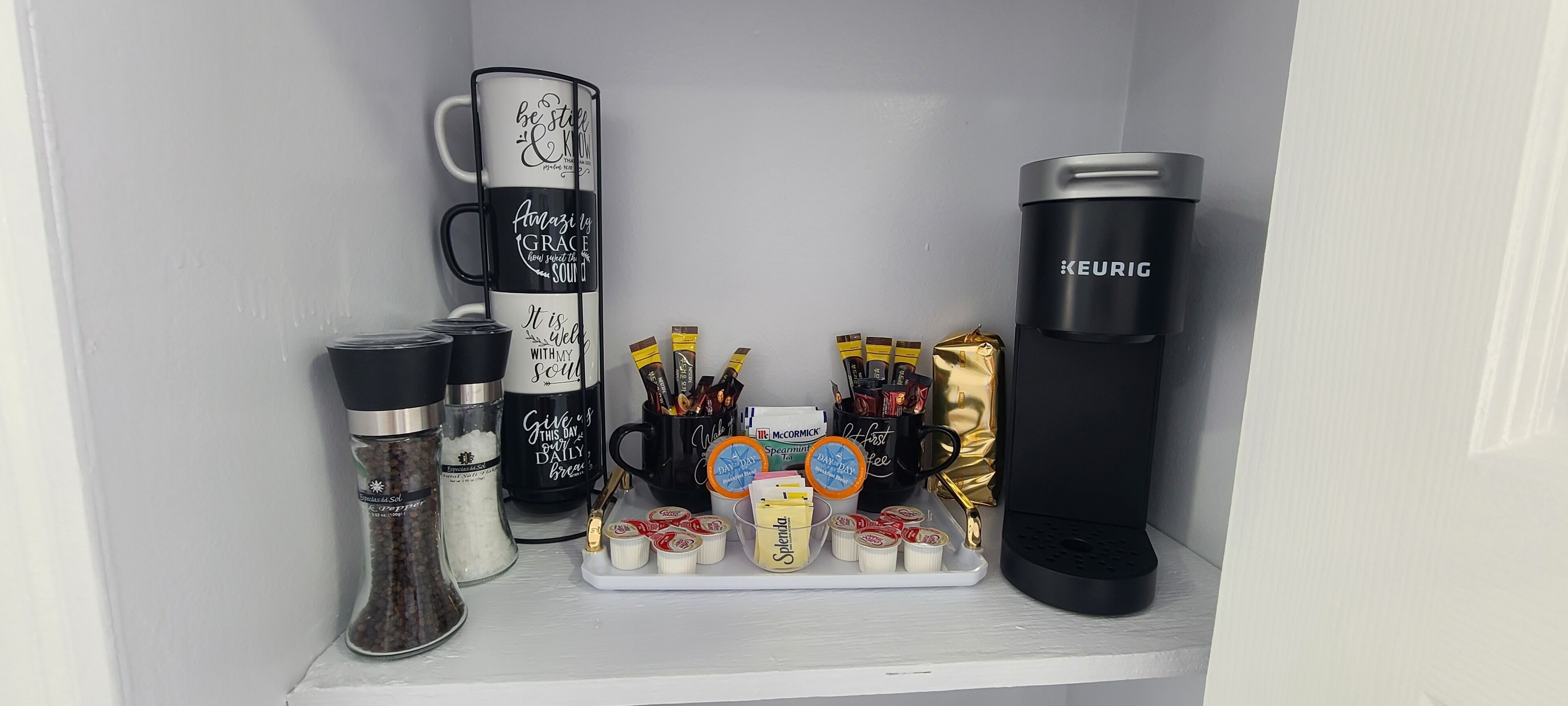 A shelf with coffee mugs, a thermos, and various coffee pods and creamer packets.