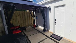 Ein überdachter Patio-Bereich mit Holzlattenzaun, einer Tür und einem Fenster.
