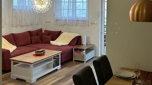 Un salon moderne avec un canapé rouge, une table à manger dressée pour deux personnes et une grande horloge murale.
