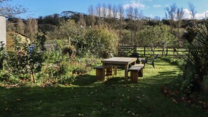 A garden with a wooden table and benches, surrounded by various plants and trees. - NEWTOWN LODGE, pet friendly in Duncannon, County Wexford (Duncannon)