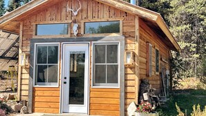 Une cabane en bois avec une porte d’entrée, deux fenêtres et une cheminée.