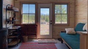 L’intérieur chaleureux d’un chalet, avec un revêtement mural en bois, une grande fenêtre, un canapé et une petite table.