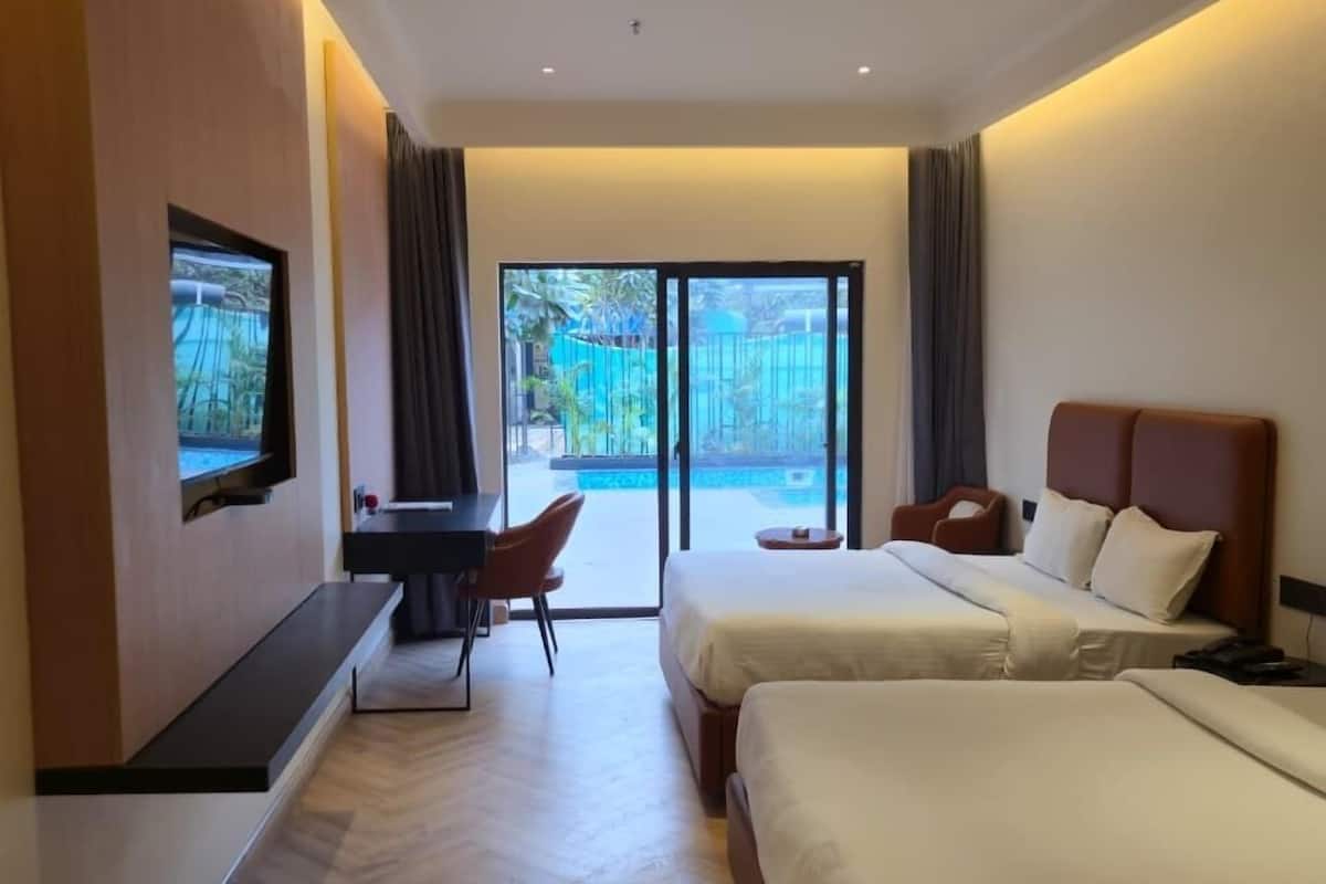Hotelkamer met twee bedden, een bureau met stoel, een aan de muur bevestigde televisie en uitzicht op een zwembad en groen.