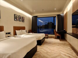 Habitación de hotel con dos camas, un escritorio y un ventanal con vistas a la ciudad de noche.