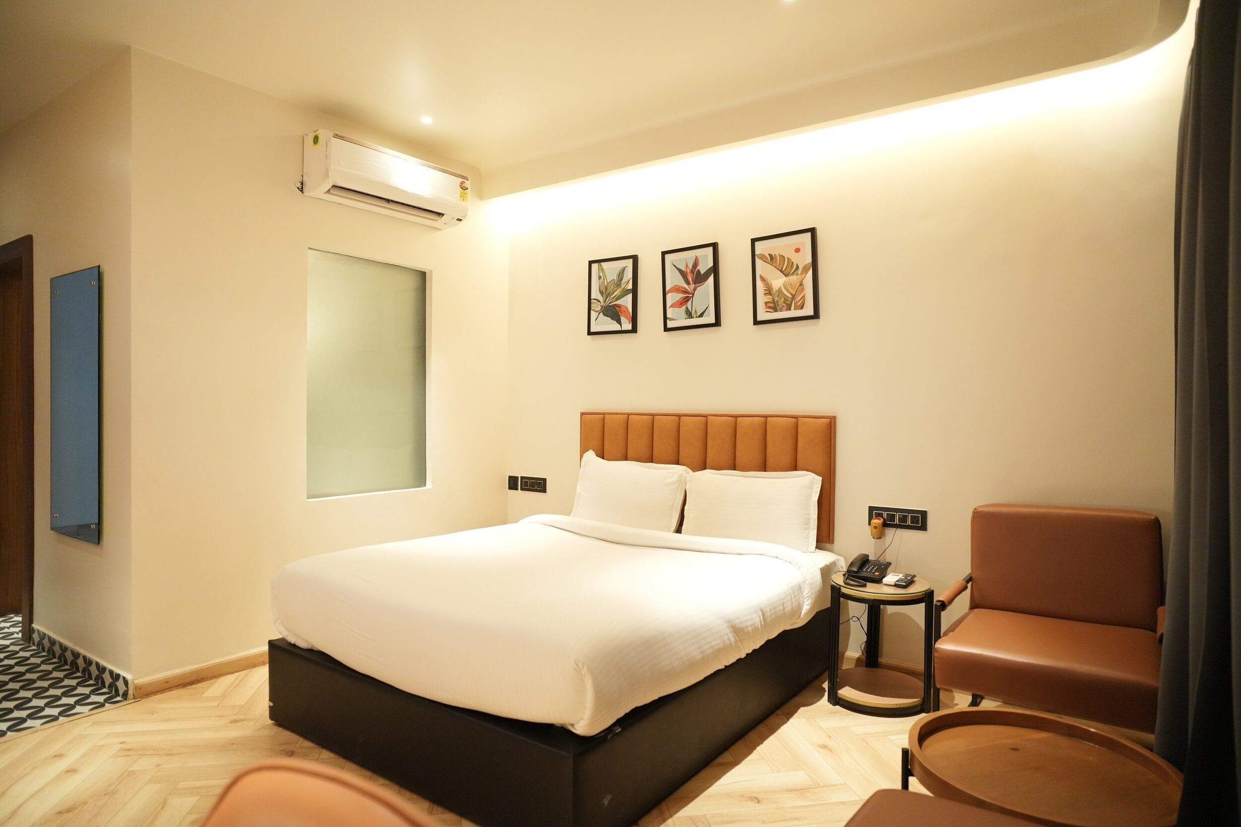 Ein modernes Hotelzimmer mit einem großen Bett, einem kleinen Beistelltisch, einem braunen Ledersessel und drei gerahmten Kunstwerken an der Wand.