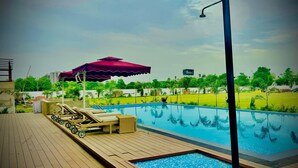 Piscina con sillas de descanso y una zona cubierta, rodeada de vegetación y un cielo despejado.