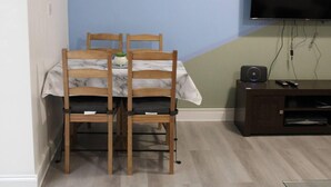 A dining area with a table set for two, a TV mounted on the wall, and a speaker on a cabinet. - Apartment - Sleeps 4 - Garden - Parking (Romford)