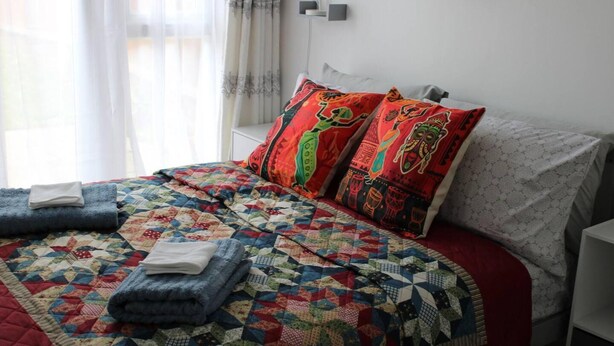 A neatly made bed with a colorful quilt, two pillows with vibrant patterns, and a folded towel on the side. - Apartment - Sleeps 4 - Garden - Parking (Romford)