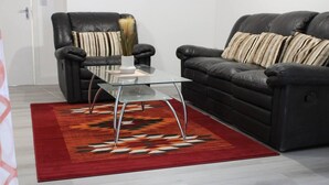 A living room with a glass coffee table, two black leather sofas, and a patterned rug. - Apartment - Sleeps 4 - Garden - Parking (Romford)