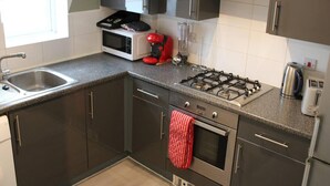 A modern kitchen with dark cabinets, a gas stove, a microwave, and a sink. - Apartment - Sleeps 4 - Garden - Parking (Romford)