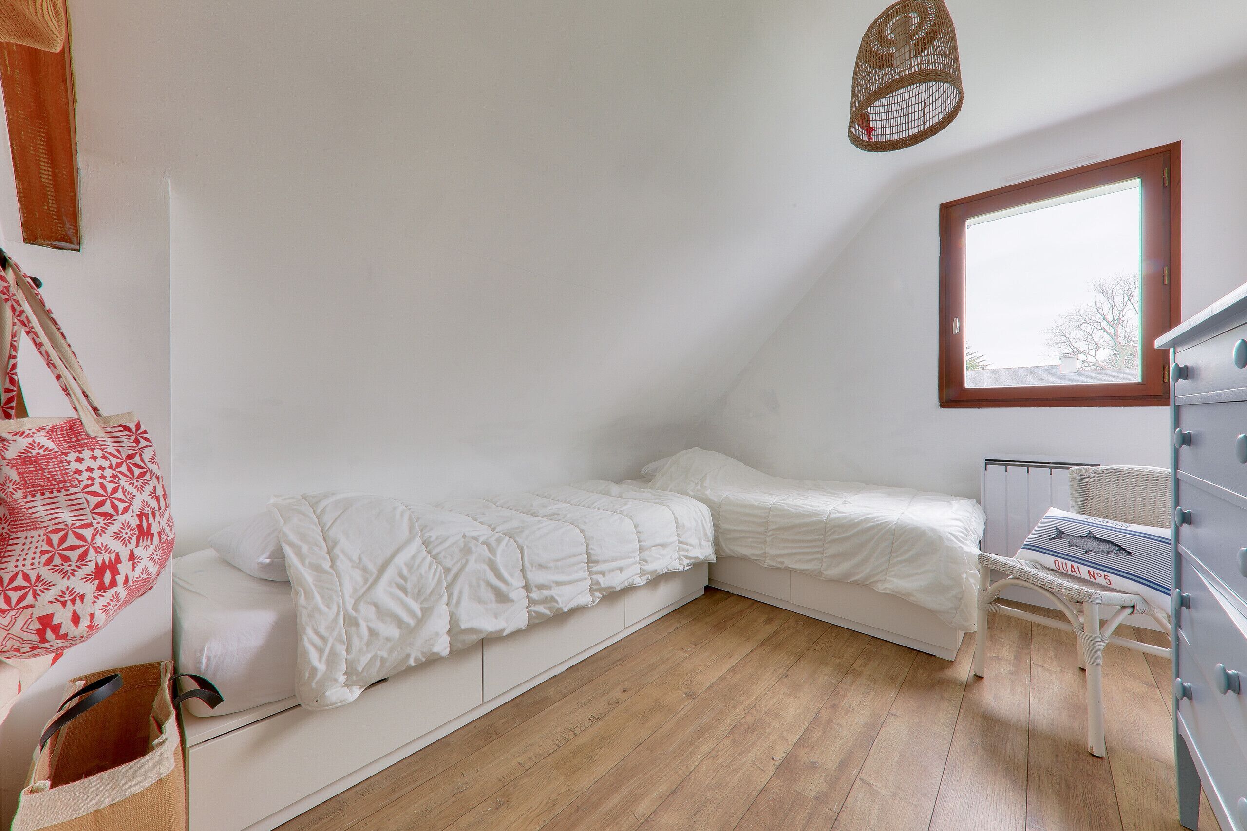 A small, tidy room with a sloped ceiling, a single bed, a chair, a dresser, and a window.