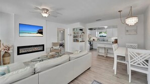 Un salon moderne avec un canapé blanc, une table basse en verre et une cheminée. On y trouve également un coin cuisine avec des meubles blancs et une table à manger entourée de chaises blanches.