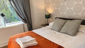 A neatly made bed with an orange bedspread and white pillows, a bedside lamp, and a window with curtains. - Impeccable 3-bed House in Nottingham Free Parking (Nottingham)