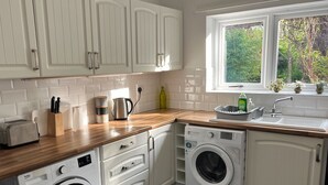 A compact kitchen with white cabinetry, a washing machine, a toaster, and a window with a view of greenery. - Impeccable 3-bed House in Nottingham Free Parking (Nottingham)
