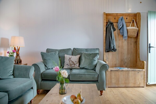 A cozy living room with a green sofa, a wooden bench, and a table with a vase of flowers and fruit. - Converted Barn with amazing views - sleeps 4 (Paignton)