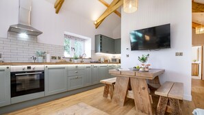 A modern kitchen with grey cabinets, a built-in oven, a wooden dining table, and a TV mounted on the wall. - Converted Barn with amazing views - sleeps 4 (Paignton)