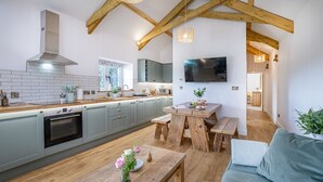 A modern kitchen with a built-in oven, grey cabinets, and a wooden dining table with benches. - Converted Barn with amazing views - sleeps 4 (Paignton)