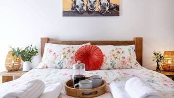 Ein ordentlich bezogenes Bett mit Blumenmuster, ein rotes Zierkissen und ein Tablett mit Teekanne und Tassen.