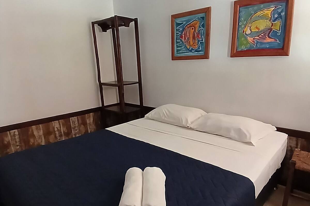 A hotel room with a bed, two paintings on the wall, and a wooden chair.