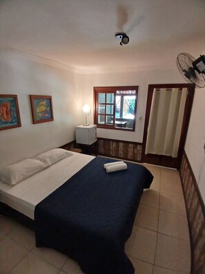 A bedroom with a bed, a nightstand, a window with curtains, and a ceiling fan. - Pousada das Palmeiras (Garopaba)