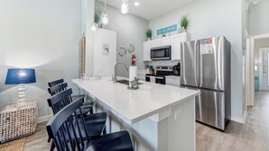 Uma cozinha moderna com armários brancos, eletrodomésticos de aço inoxidável e uma ilha central com banquetas.
