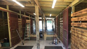 A stable with wooden walls and a central aisle, featuring black mats on the floor and a ladder. - R/V spots on working horse farm $85 per night/$850 dollars per mo (Citra)