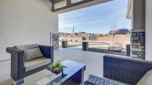Ein Patio im Freien mit Korbmöbeln, einem Glastisch und Blick auf eine Wohngegend.
