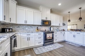A modern kitchen with white cabinets, a stainless steel oven, a microwave, and a granite countertop. - Cedar City Home w/ Mountain Views + Hiking Trails! (Cedar City)