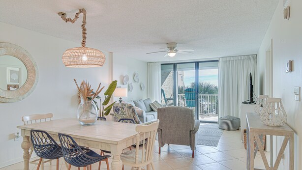 A dining area with a white table, blue chairs, and a hanging light fixture. - Orange Beach Condo w/ Beach+ Tennis Court Access (Orange Beach)