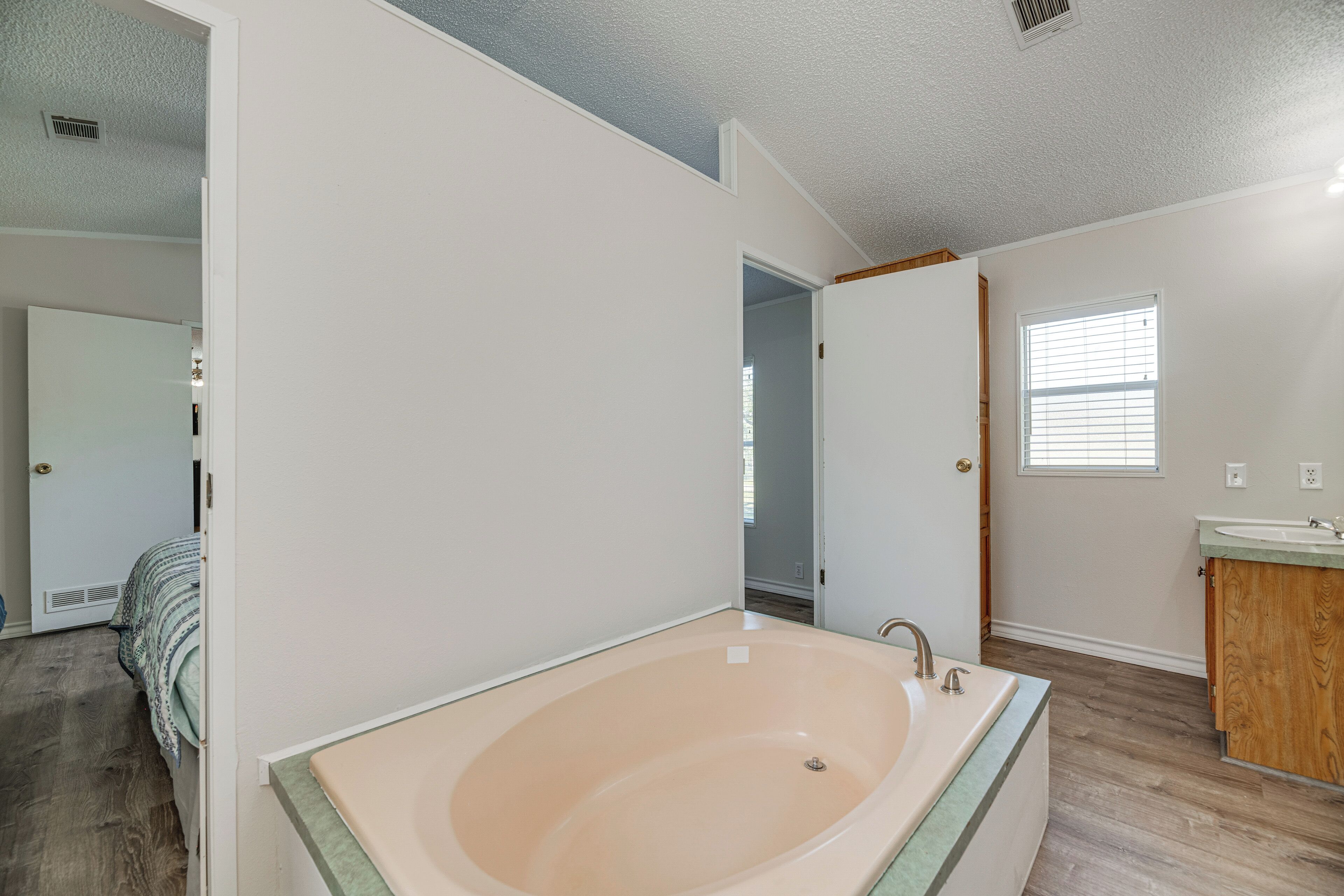 A bathroom with a large bathtub, a wooden vanity, and a window with blinds.
