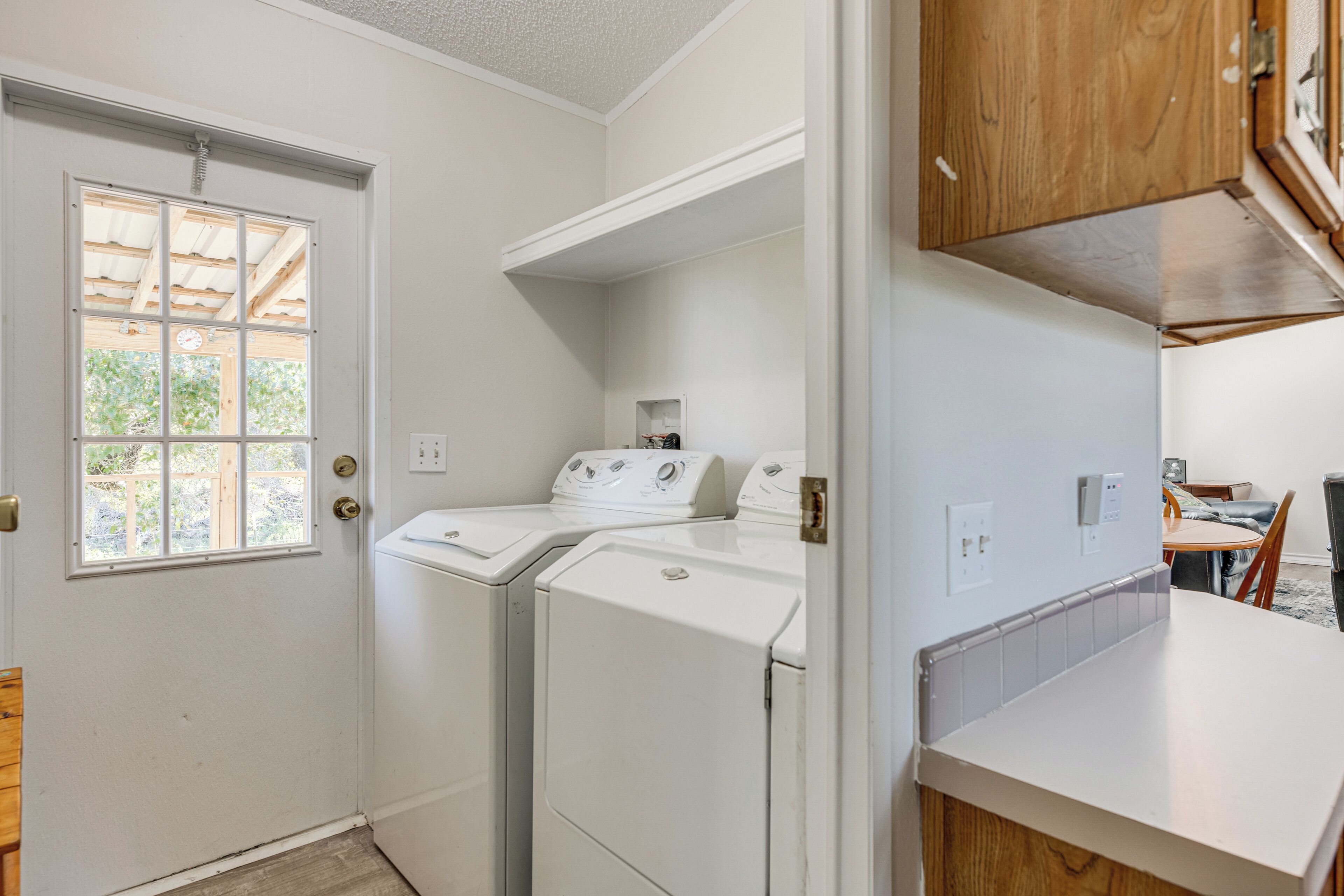 A laundry room with two white front-loading washers and dryers, a wooden cabinet, and a white countertop.