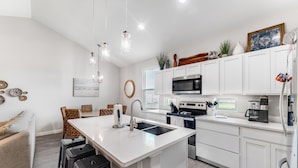 A modern kitchen with white cabinetry, a central island with a sink, stainless steel appliances, and pendant lighting.