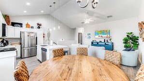 A modern kitchen with stainless steel appliances, a dining area with a wooden table, wicker chairs, and a ceiling fan.