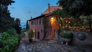 A stone-paved courtyard with a pink building, potted plants, and a stone wall. - Casa del Duca 10, Emma Villas (Portoferraio)