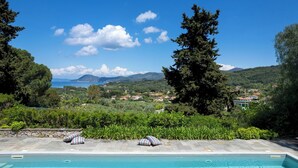 A pool with lounge chairs and pillows, surrounded by lush greenery and a view of a coastal town. - Casa del Duca 10, Emma Villas (Portoferraio)